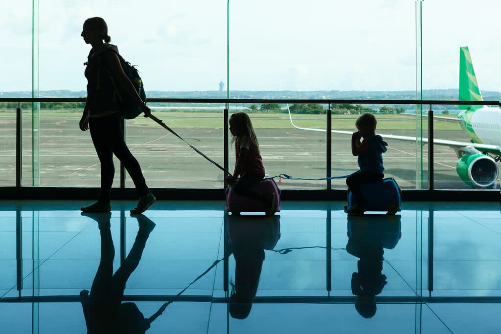 In airport transit hall young mother carries on suitcases little kids to departure gate for boarding to airplane. Active family lifestyle, travel by air with children on summer vacation